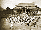 "Boys and girls of Shuri City Elementary School: martial arts performance with instructor Shinpan Shiroma, in 1937" - Shuri Castle.